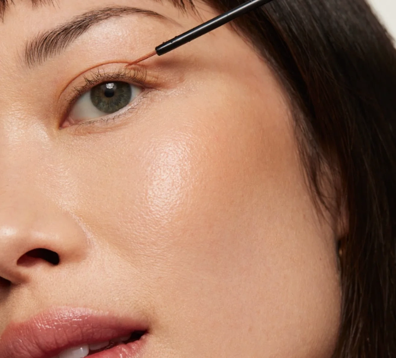 Close-up of a woman applying UKLASH eyelash serum along her upper lash line with a fine brush.