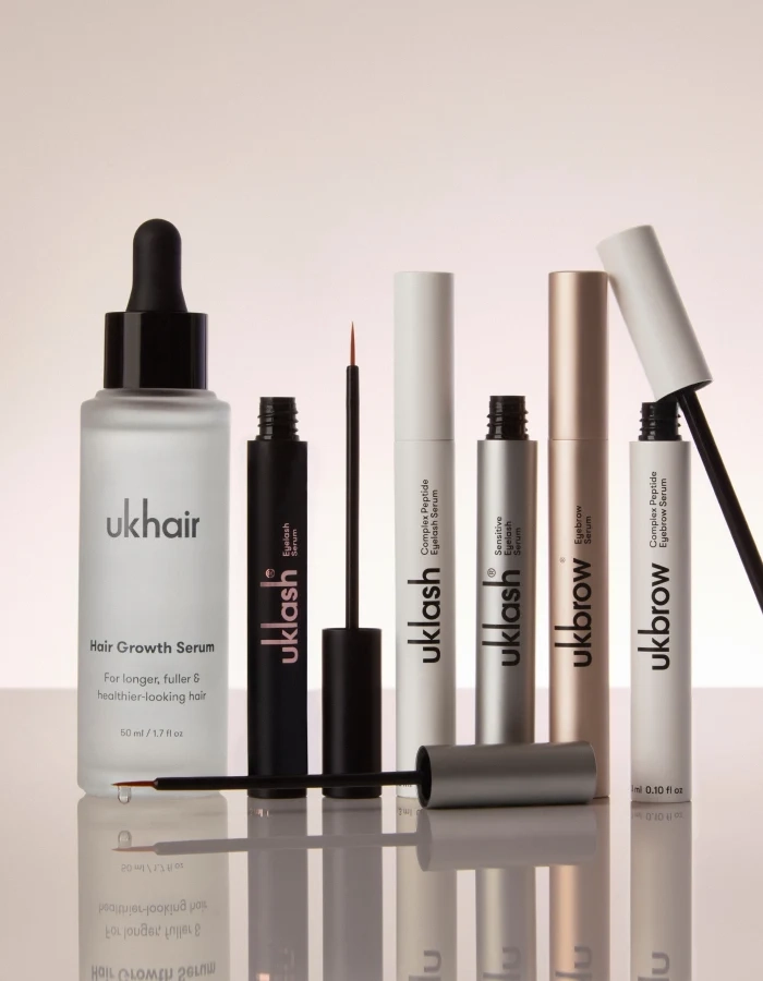 UKHAIR Hair Growth Serum with UKLASH and UKBROW eye products, including mascara and serums, displayed on a reflective surface.